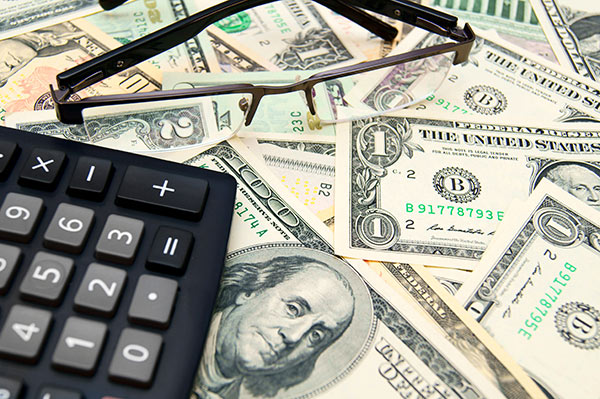 Glasses and a calculator on a pile of US dollars.